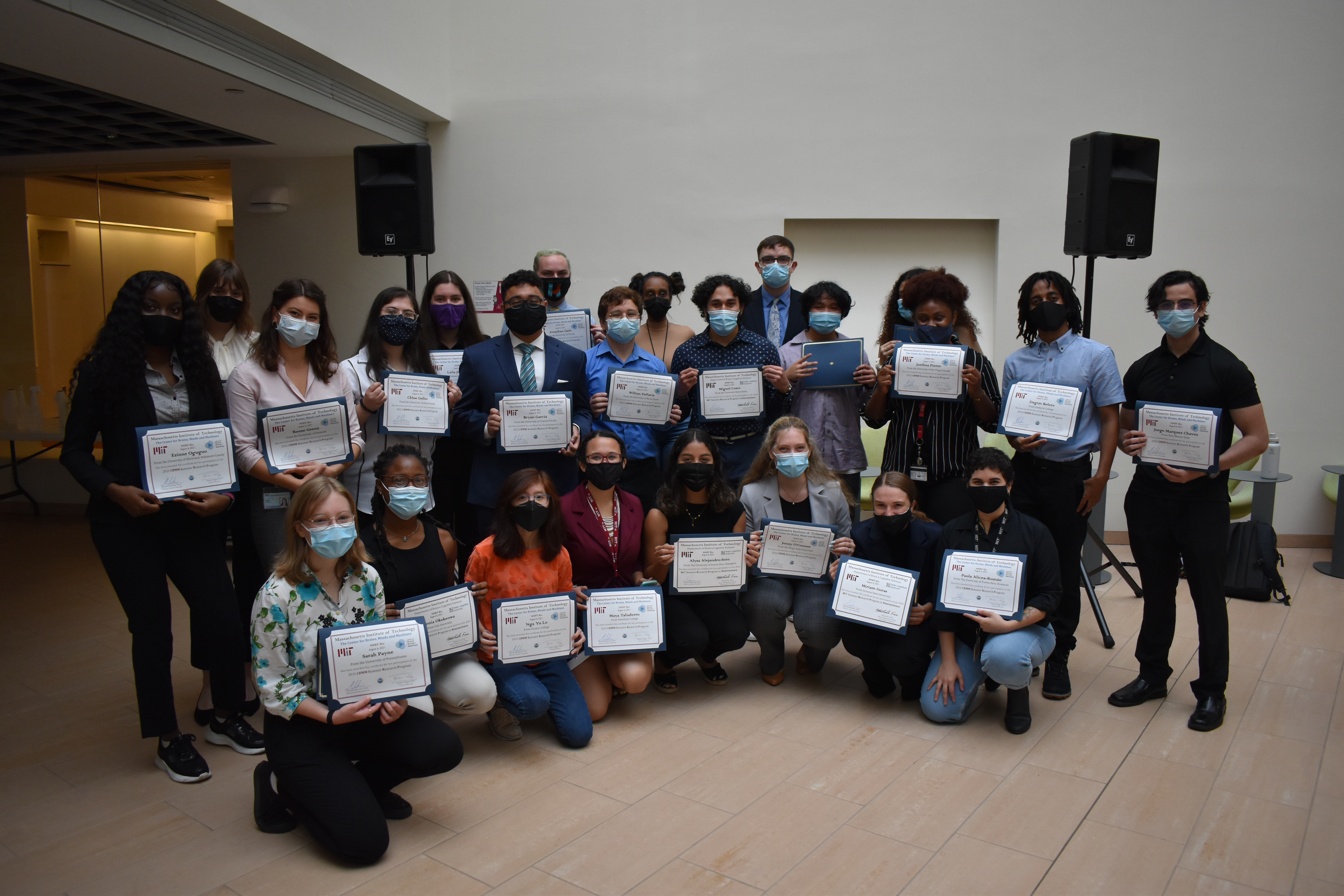 Two rows of students, one standing and one kneeling, hold certificates.