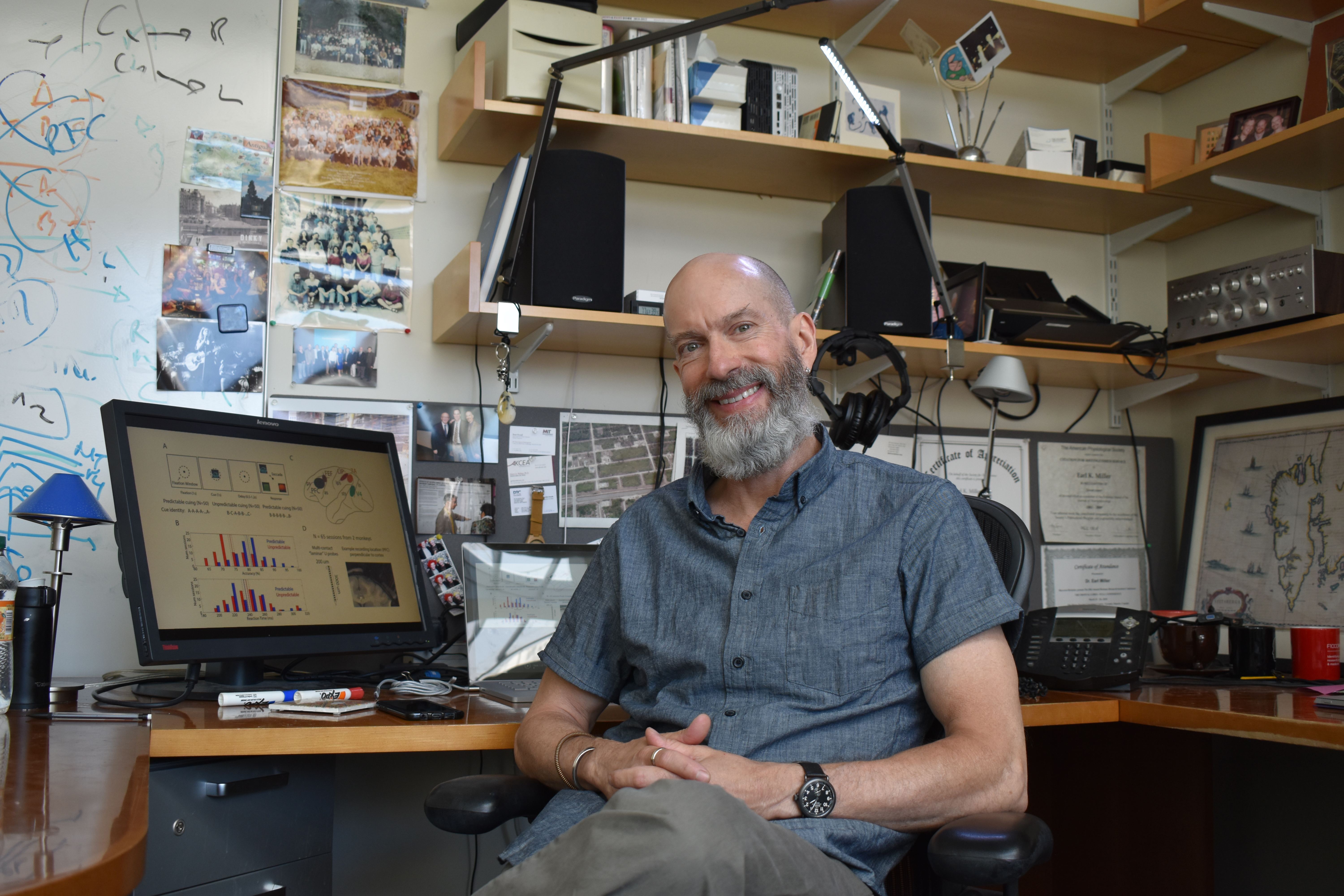 Earl Miller sits smiling at his desk with data on his computer screen