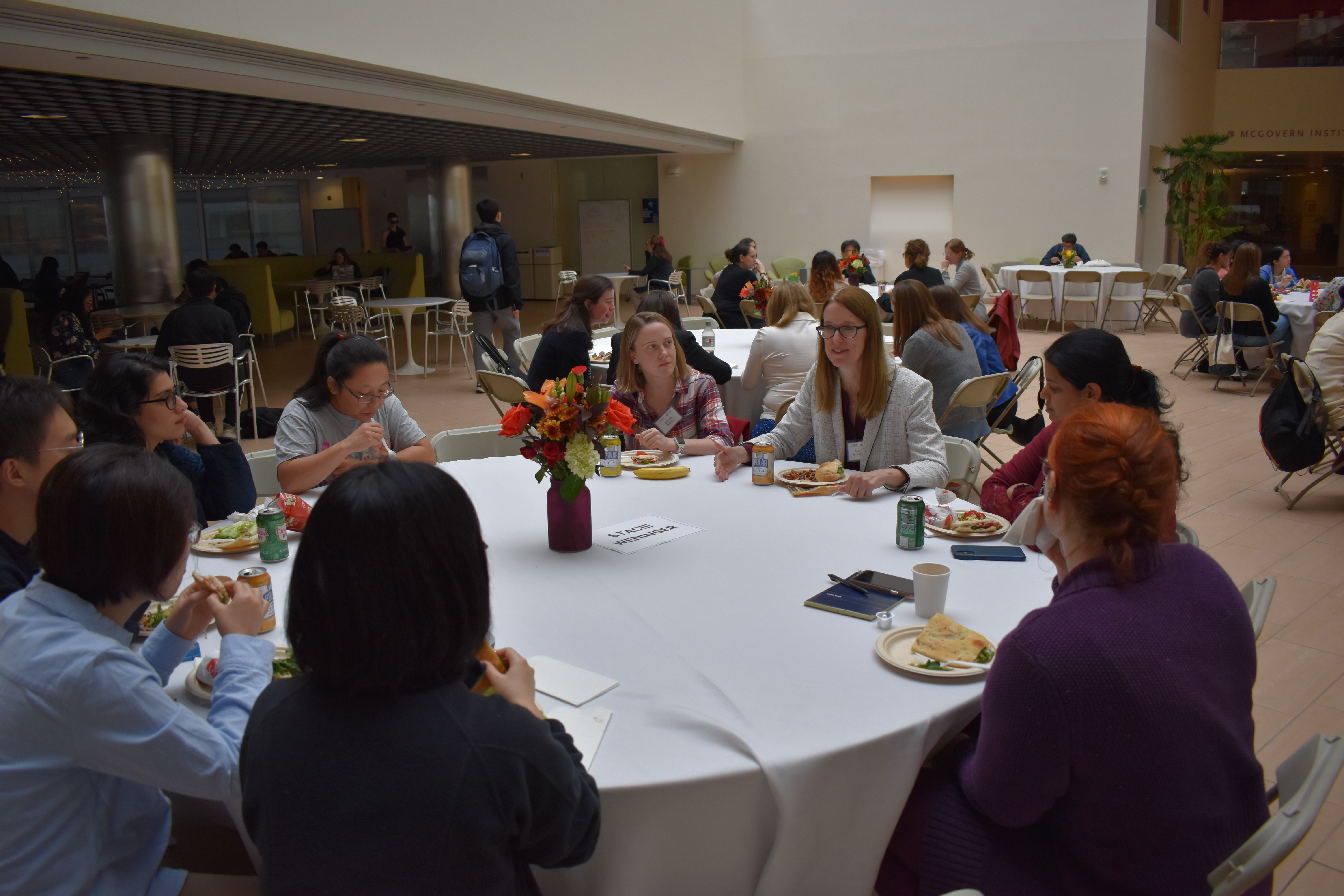 People sit around a round table in the spacious atrium of MIT Building 46. Stacie Weninger smiles as she speaks to the group.