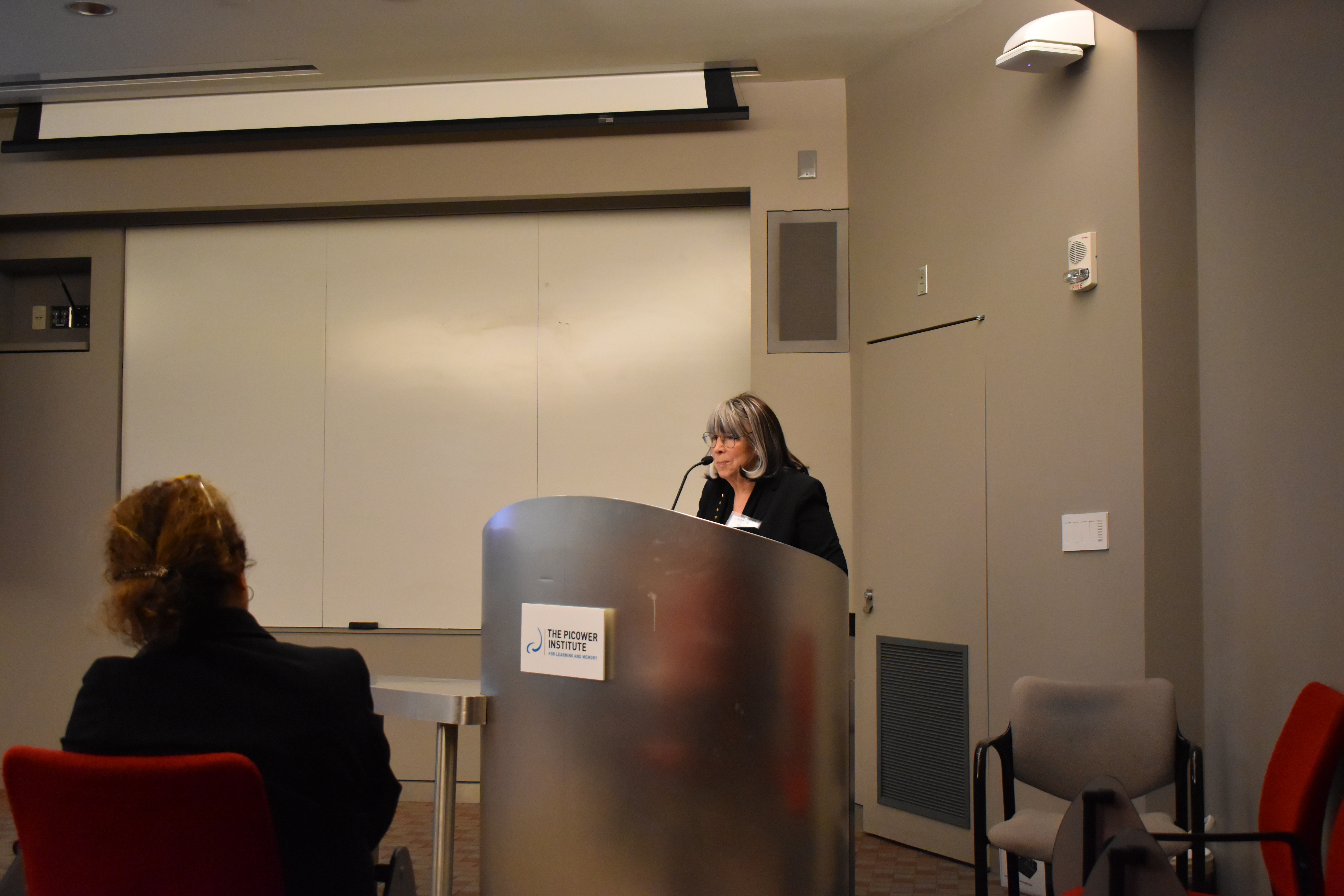 Susan Silbey stands behind a silvery podium in the Picower Seminar Room of MIT Building 46.