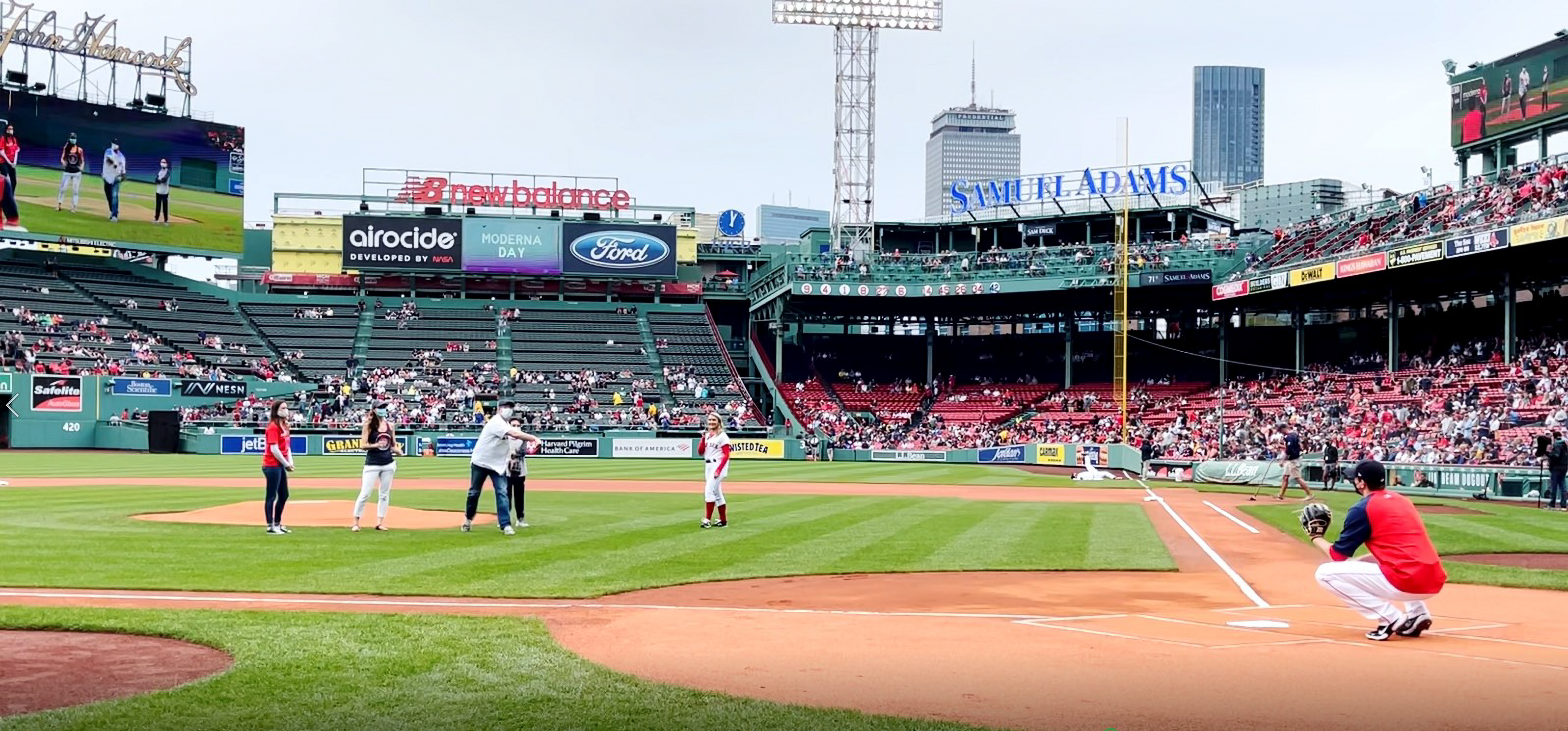 A view from the third base line at Fenway shows five people standing near the mound. One has thrown a ball that's on the way to the catcher.