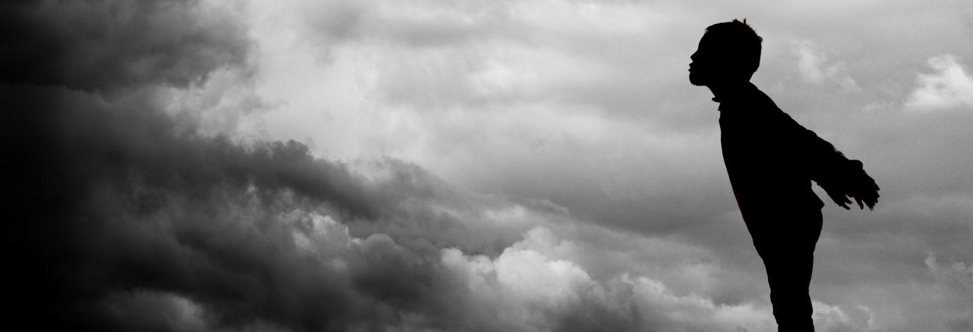 Silhouette of a child leaning toward a dark cloudmass, as if blowing the dark clouds away