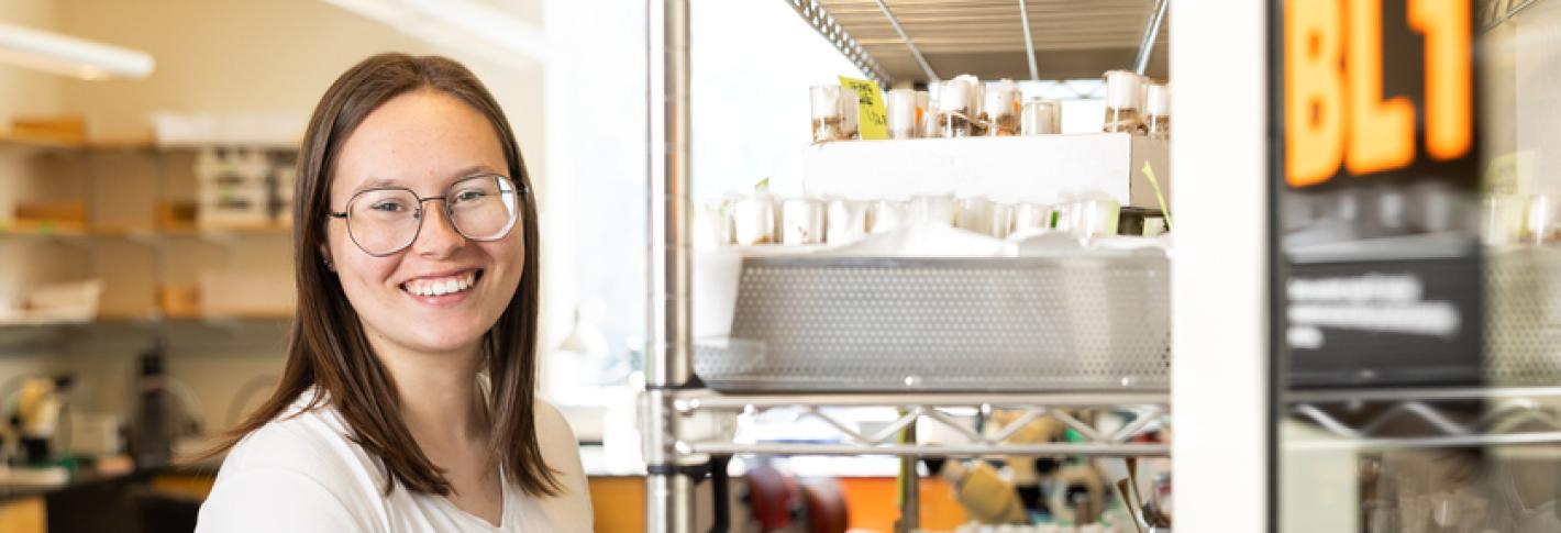 Payton Dupuis stands next to a set of shelves holding a box with a large number of cotton-topped vials containing flies.