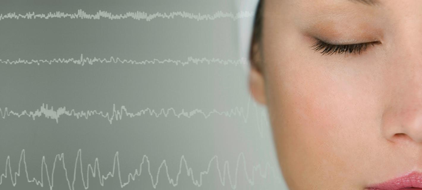 A closeup on the right half of a sleeping woman's face is flanked on her right (our left) with white brainwaves extending across the image over a grey background